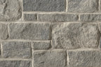 Mur en pierre grise avec des blocs de différentes tailles, présentant une texture rugueuse et des joints clairs entre les pierres.