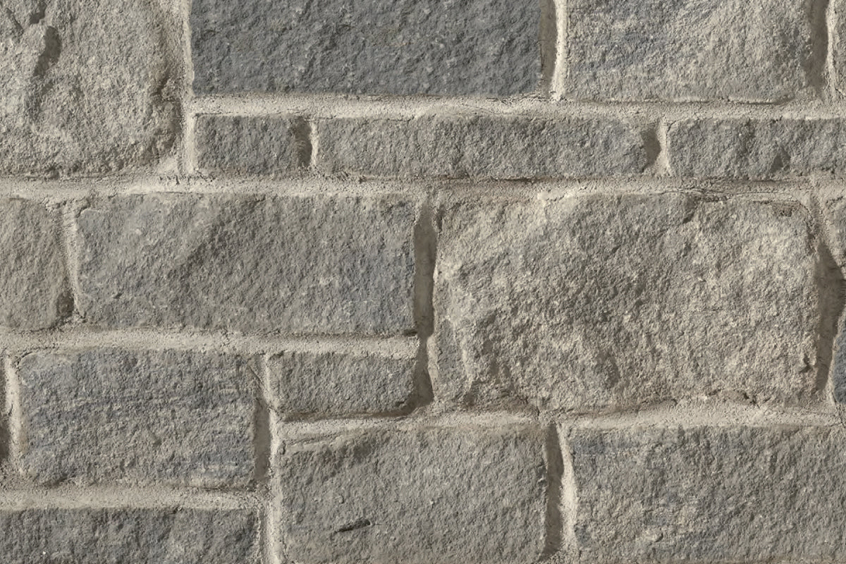 Mur en pierre grise avec des blocs de différentes tailles, présentant une texture rugueuse et des joints clairs entre les pierres.