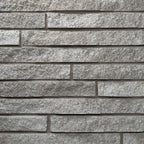 Mur en pierre grise avec des blocs rectangulaires disposés horizontalement, créant une texture rugueuse et moderne.