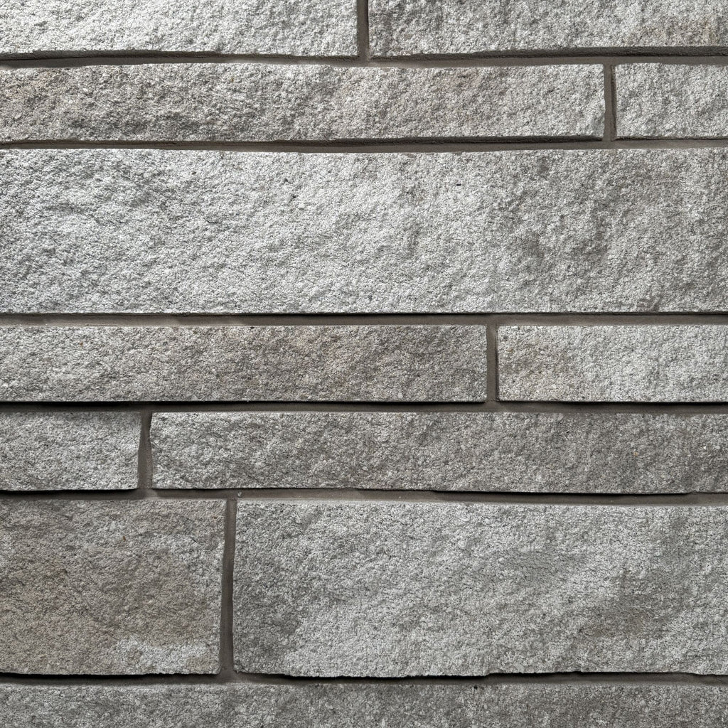 Mur en pierre grise avec des blocs de différentes tailles et textures, créant un motif de maçonnerie.