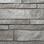 Mur en pierre grise avec des blocs de différentes tailles et textures, créant un motif de maçonnerie.