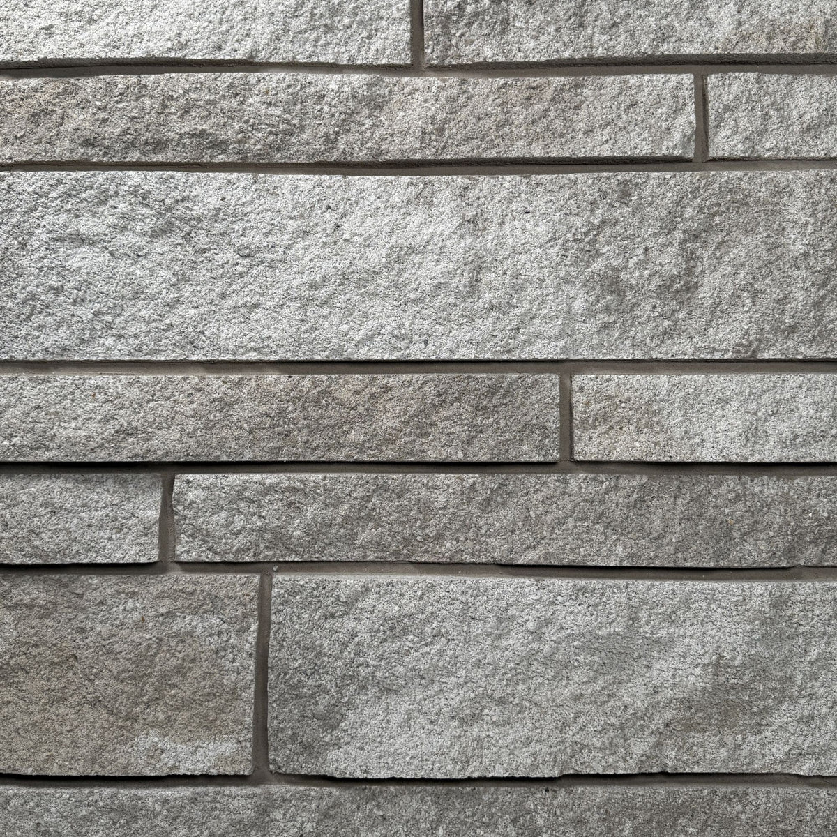 Mur en pierre grise avec des blocs de différentes tailles et textures, créant un motif de maçonnerie.