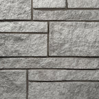 Mur en pierre grise avec des blocs rectangulaires texturés, créant un motif de maçonnerie.