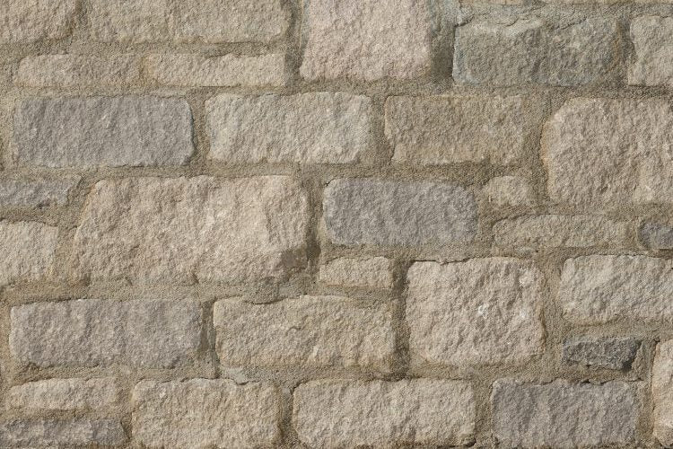 Mur en pierre avec des blocs de différentes tailles et teintes, allant du gris clair au beige, texture rugueuse.