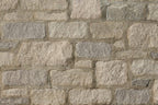 Mur en pierre avec des blocs de différentes tailles et teintes, allant du gris clair au beige, texture rugueuse.