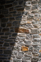 Mur en pierre avec des nuances de gris et d'orange, montrant des textures variées et des ombres.