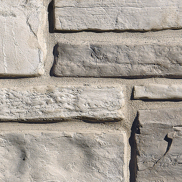 Mur en pierre grise avec des textures variées, présentant des blocs de pierre de différentes tailles et finitions.