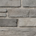 Briques en pierre grise de différentes tailles, disposées en motif sur un mur, avec un fond de sable.