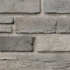 Briques en pierre grise de différentes tailles, disposées en motif sur un mur, avec un fond de sable.