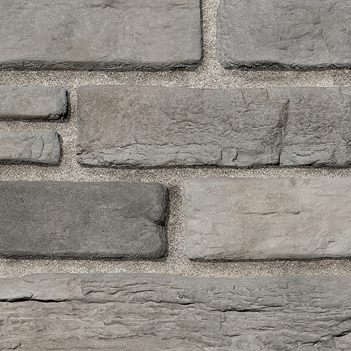 Briques en pierre grise de différentes tailles, disposées en motif sur un mur, avec un fond de sable.