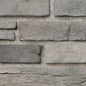 Briques en pierre grise de différentes tailles, disposées en motif sur un mur, avec un fond de sable.
