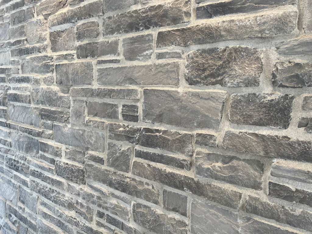 Mur en pierre grise avec des textures variées, présentant des blocs de différentes tailles et formes.