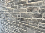 Mur en pierre grise avec des textures variées, présentant des blocs de différentes tailles et formes.