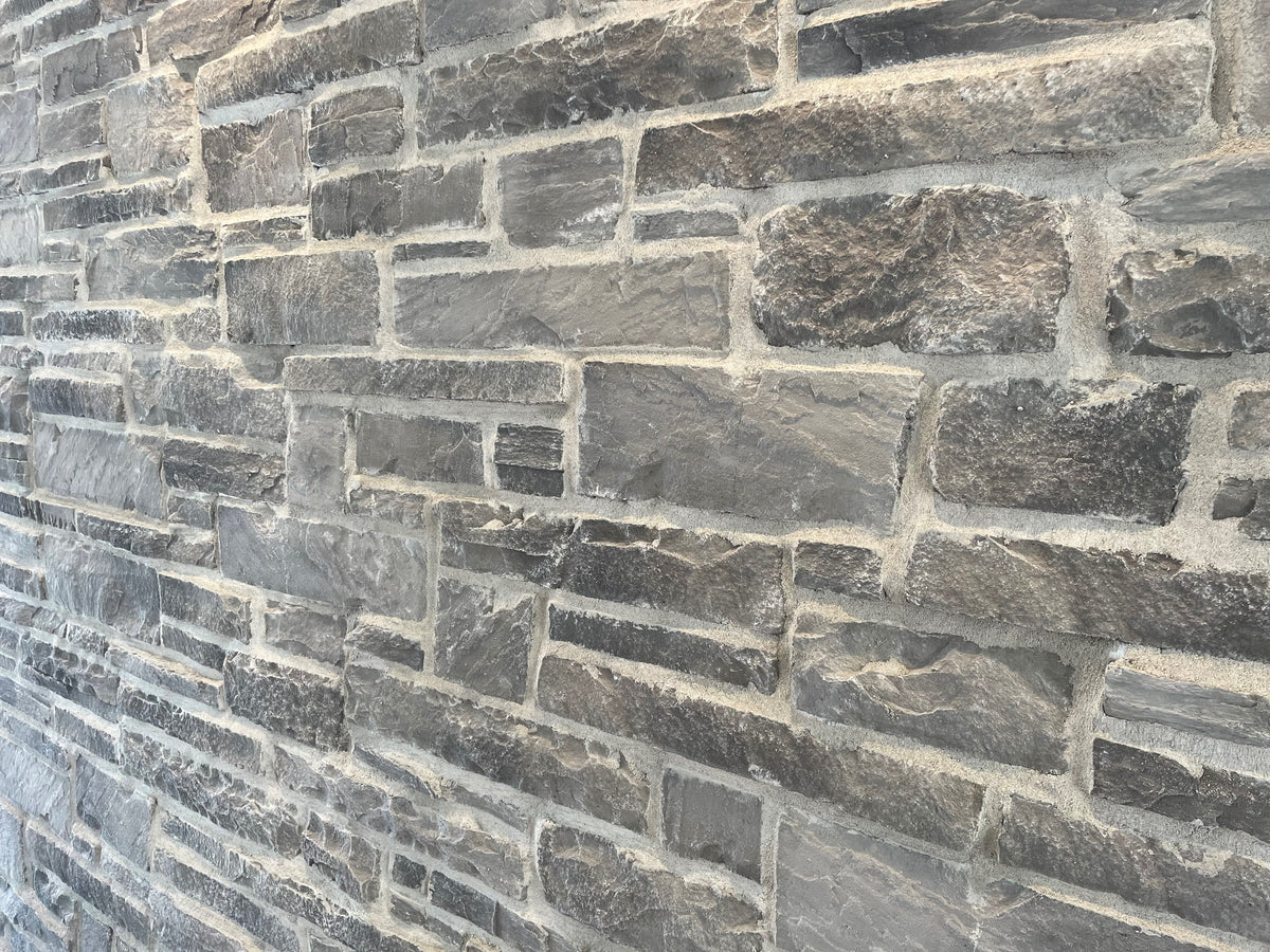 Mur en pierre grise avec des textures variées, présentant des blocs de différentes tailles et formes.