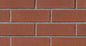 Mur en briques rouges avec des joints gris, texture rugueuse et uniforme, disposé en motif rectangulaire.