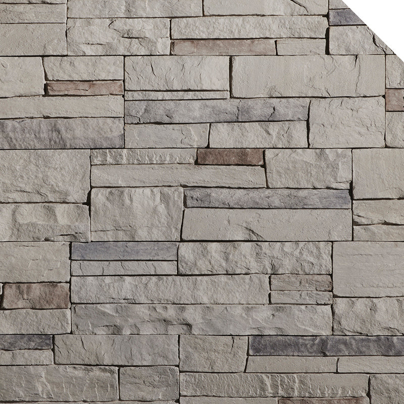 Mur en pierre décorative avec des blocs de différentes teintes de gris et quelques touches de brun, texture rugueuse.