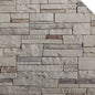 Mur en pierre décorative avec des blocs de différentes teintes de gris et quelques touches de brun, texture rugueuse.