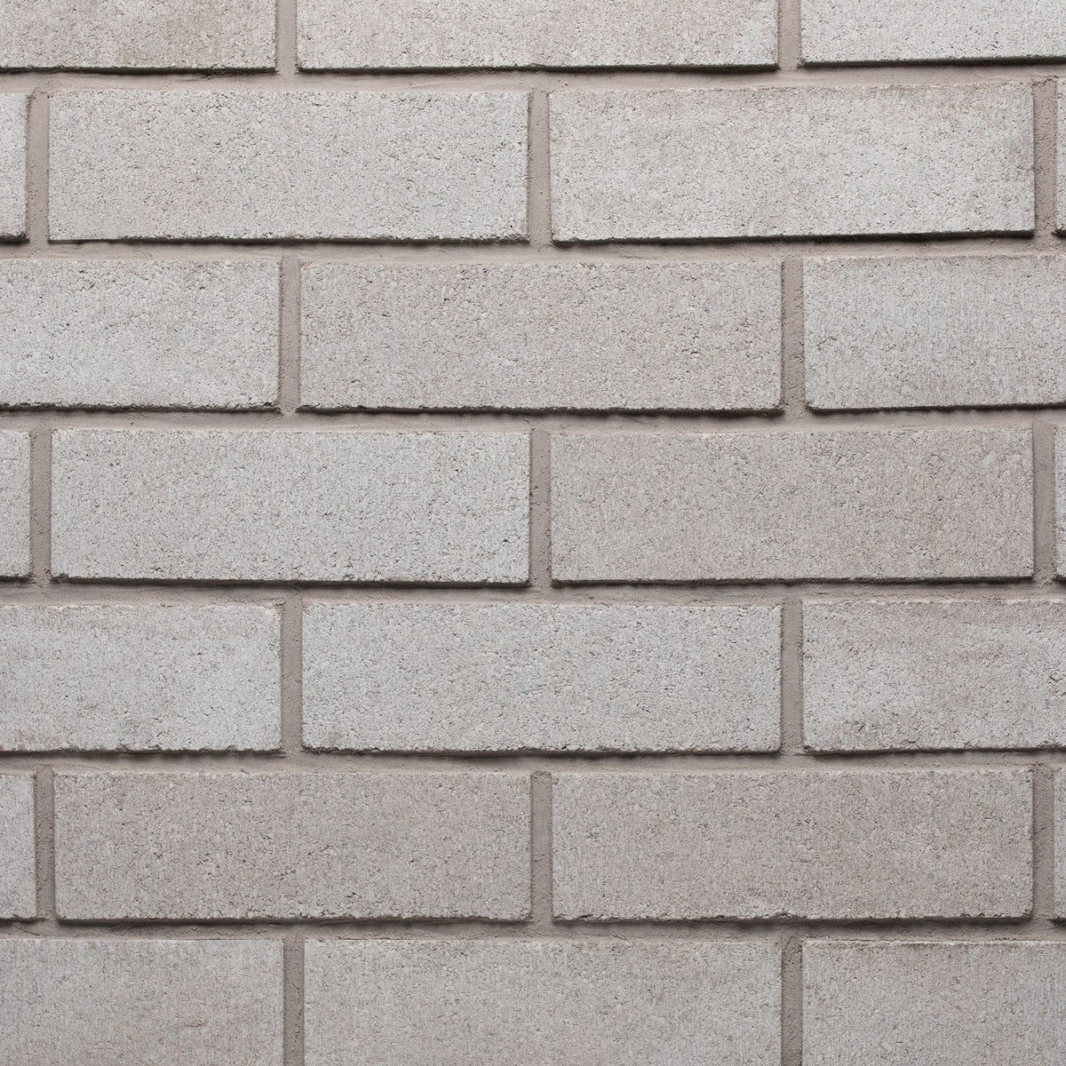 Mur en briques grises, texture lisse, disposées en rangées régulières, avec des joints clairs entre chaque brique.