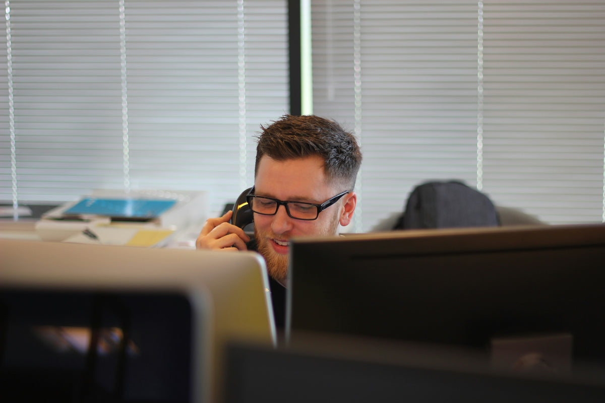Homme souriant au telephone dans un bureau avec ordinateurs.