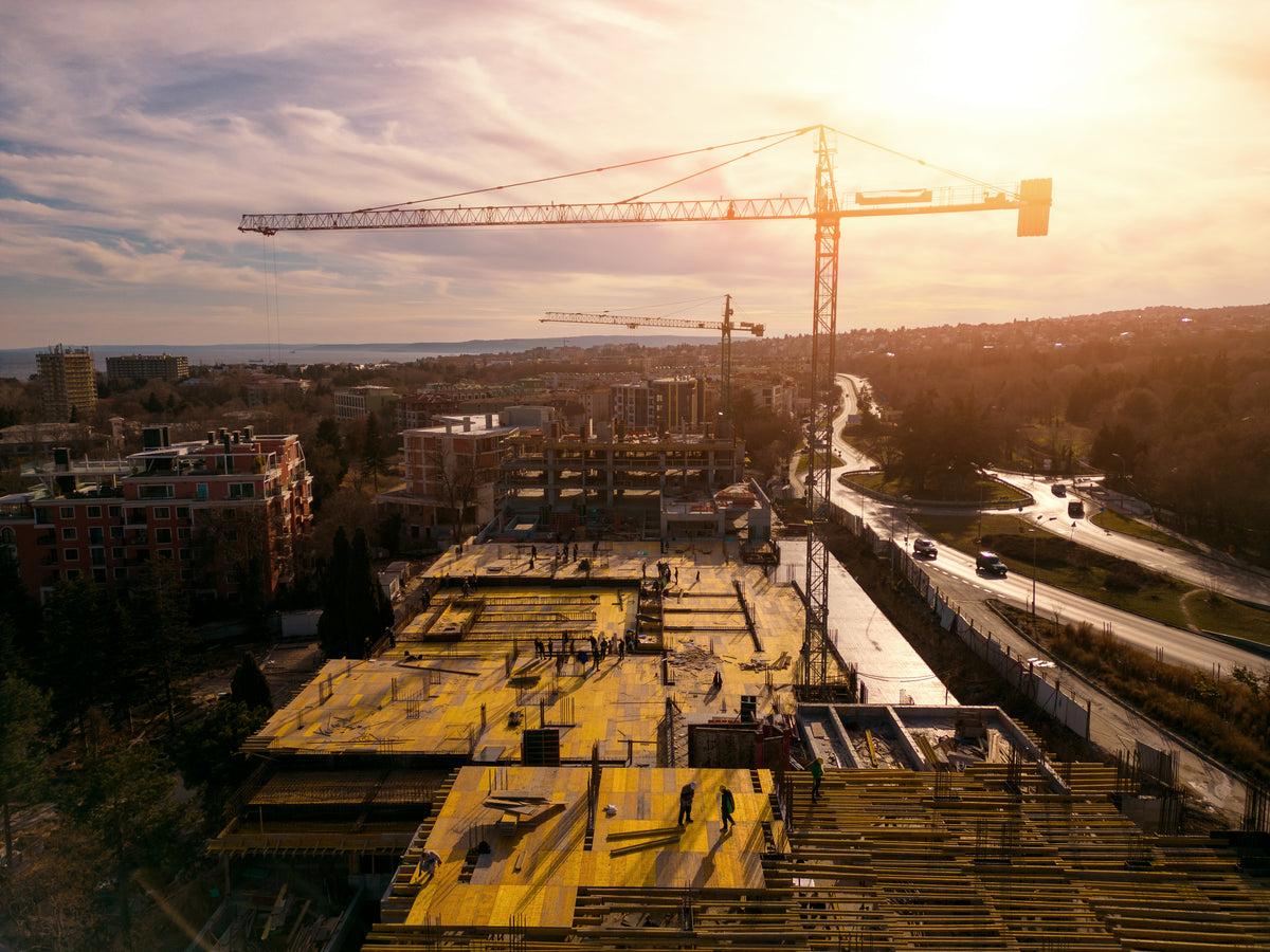 Chantier de construction avec des ouvriers, grues, et bâtiments en cours d'édification sous un ciel ensoleillé.
