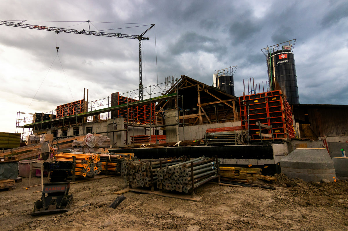 Chantier de construction avec échafaudages, matériaux de construction, et réservoirs sur fond de ciel nuageux.
