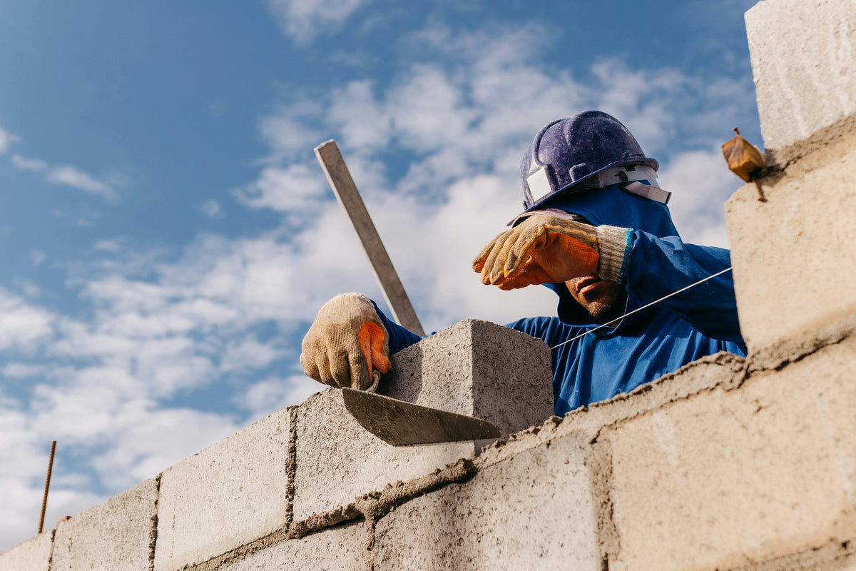 Ouvrier casque et gants posant des blocs de beton sous un ciel nuageux.