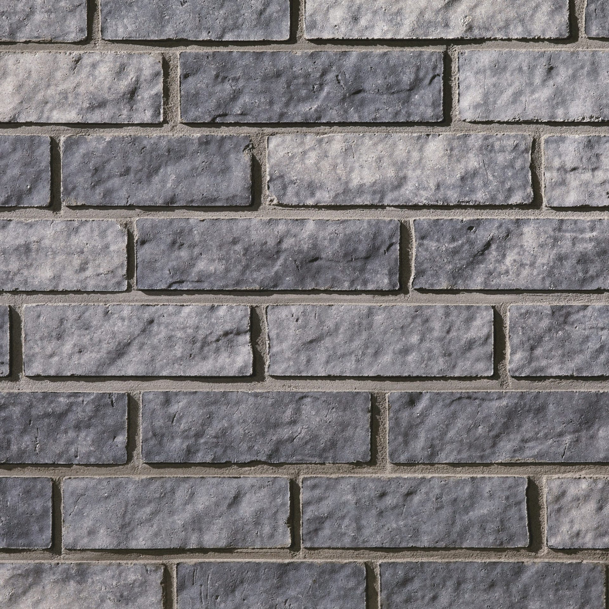 Mur de briques en pierre grise, avec des textures et des nuances variées, disposées en motifs rectangulaires.