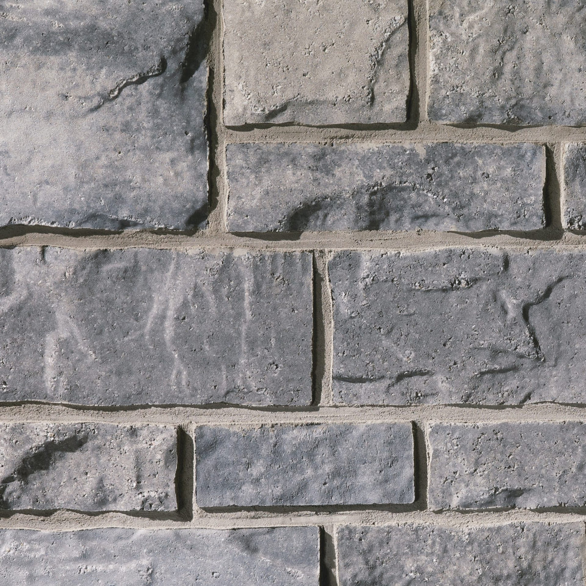 Mur en pierre grise avec des blocs de différentes tailles et textures, présentant des nuances de gris et des joints clairs.