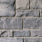 Mur en pierre grise avec des blocs de différentes tailles et textures, présentant des nuances de gris et des joints clairs.