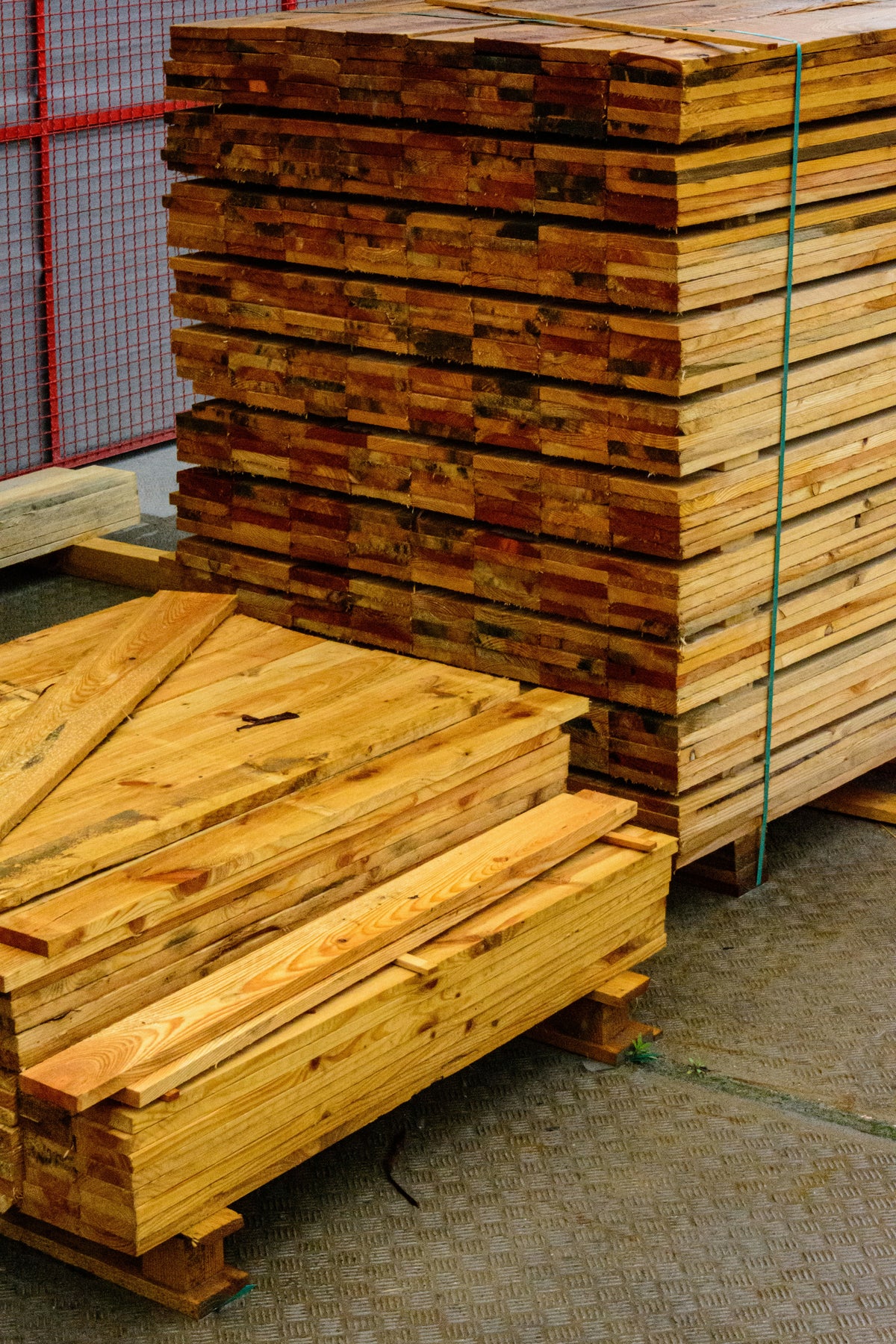 Piles de planches en bois empilées, avec des planches plus petites en avant, sur un sol en béton.