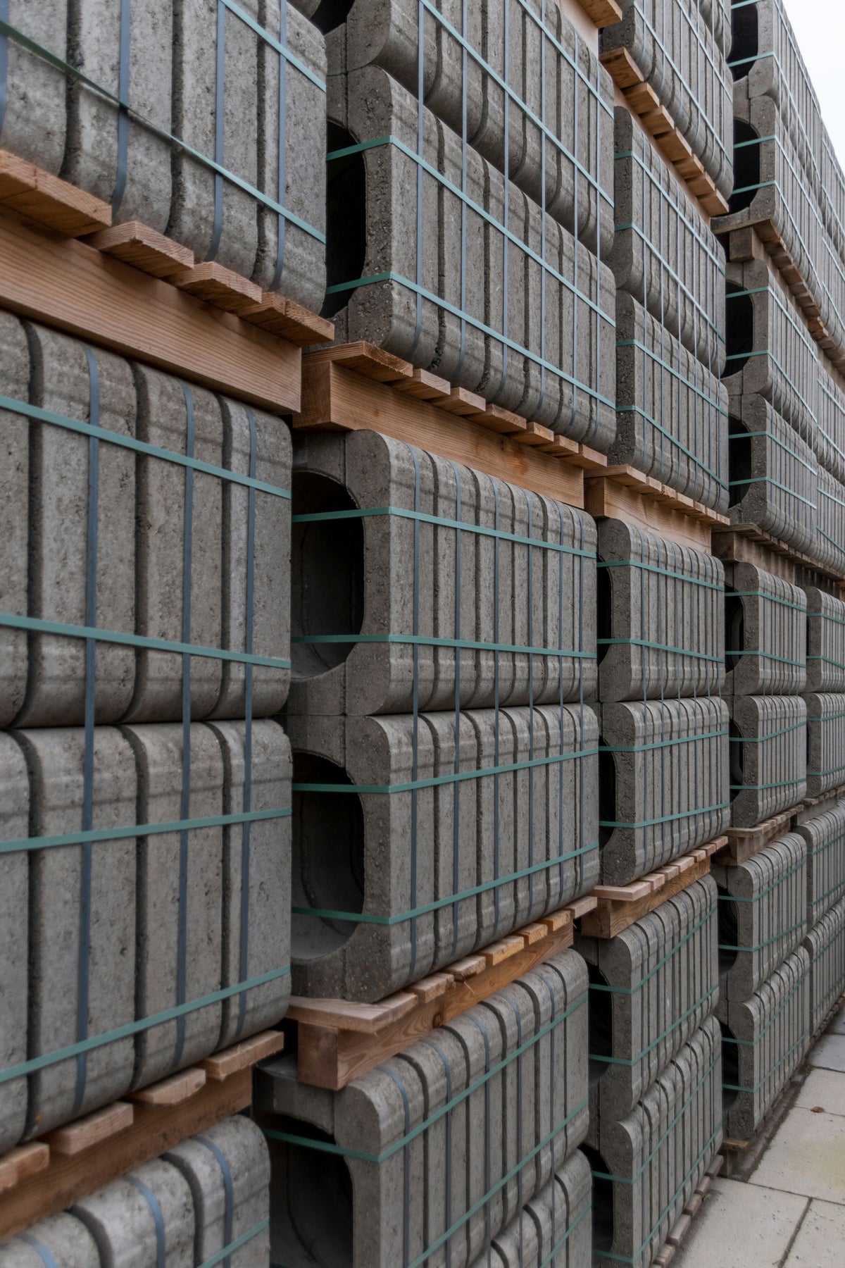 Blocs de béton empilés sur des palettes en bois, attachés avec des bandes élastiques, dans un environnement extérieur.